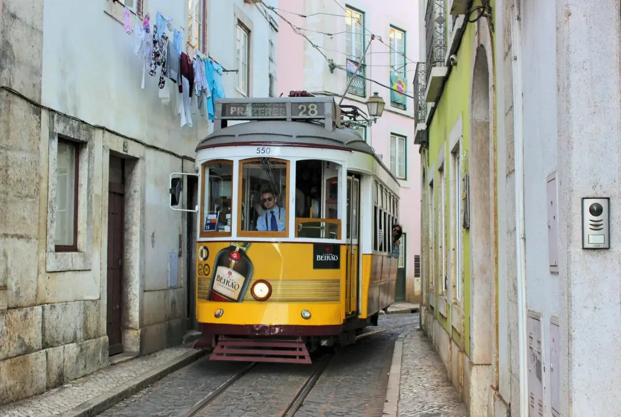 Gelbe straßenbahn lissabon fährt durch enge Gasse, Wäsche hängt über der Straße.