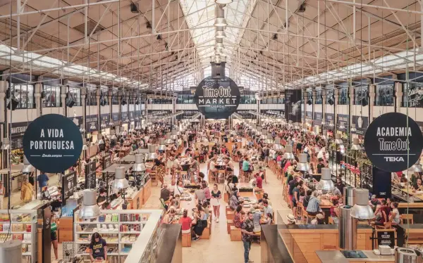 Belebter Time Out Market in Lissabon. Menschen sitzen an langen Tischen, essen und unterhalten sich. Überall gibt es Essensstände.