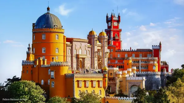 Buntes Sintra Pena Palace mit gelben und roten Türmen, einer blauen Kuppel und einem Uhrenturm unter blauem Himmel.