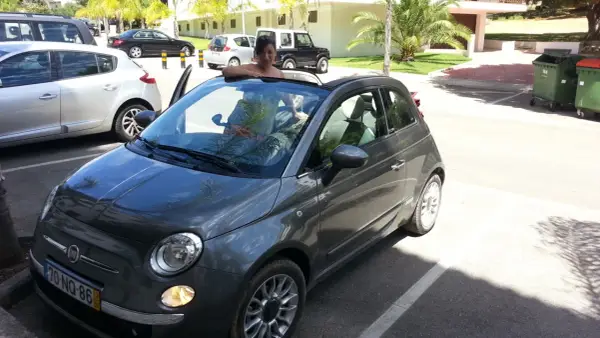 Frau lehnt sich aus einem grauen Fiat 500 Cabrio, bereit für eine Spritztour. Hier sind einige mietwagen portugal tipps für Ihren Urlaub!