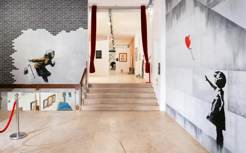 Banksy Lissabon: ikonische Werke wie das Mädchen mit dem roten Ballon und die wegspritzende Frau zieren die Wände einer Ausstellung.